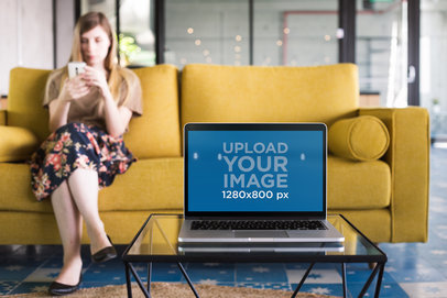 Mockup of a MacBook Standing on a Glass Table Near a Woman
