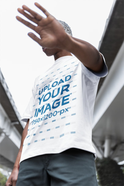 Oversized T-Shirt Mockup of a Man Posing in the Street While Covering His Face