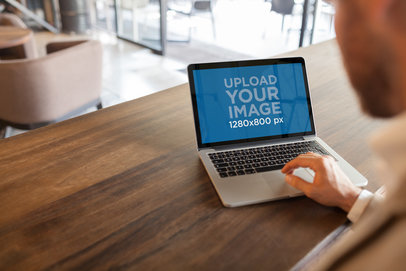 Mockup of a Businessman Using a MacBook on a Wooden Table