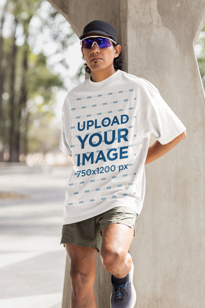 Oversized T-Shirt Mockup of a Serious Man With Running Clothes Leaning on a Concrete Column
