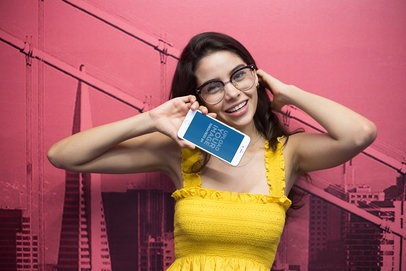Mockup of a Happy Woman Holding an iPhone Against a Pink Printed Wall a21448