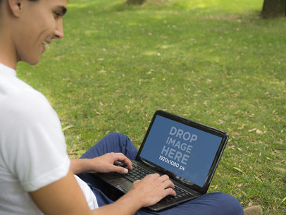 Young Man Sitting on Grass in Park and Using an HP Laptop
