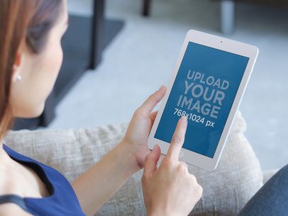 Mockup of a Beautiful Woman Sitting on Couch Using iPad Mini 
