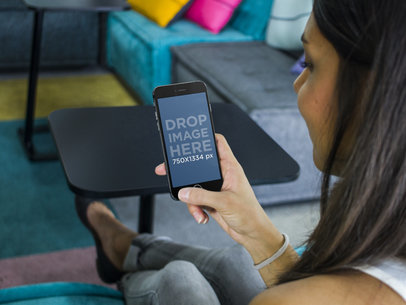 Mockup of a Young Lady Sitting at a Lounge and Using a Black iPhone