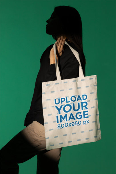Mockup of a Mysterious Woman Holding a Tote Bag in a Studio with Customizable Background m50042