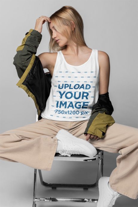 Mockup of a Woman Sitting on a Chair in a Studio While Wearing a Bella Canvas Tank Top
