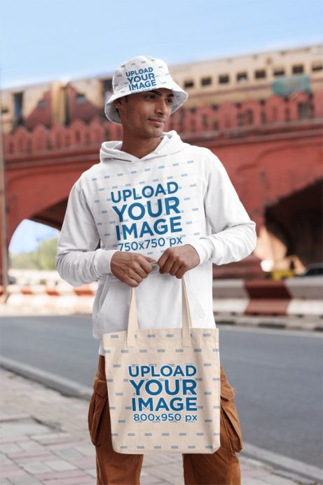 Gildan Hoodie Mockup of a Gen-Z Man With a Bucket Hat and a Tote Bag