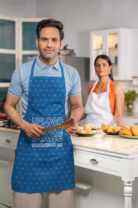 Kodenipr Club Apron Mockup of a Confident Man With a Cooking Spoon Posing With His Wife in a Kitchen