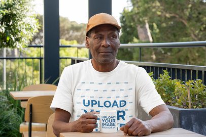 Bella Canvas Tee and Mug Mockup of an Elderly Man Sitting in an Outdoor Restaurant m51507