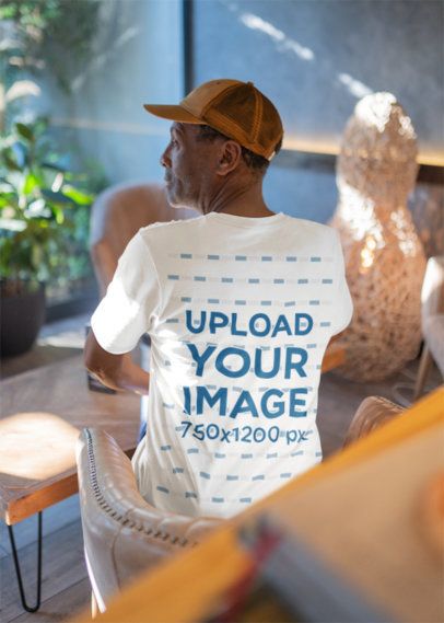 Bella Canvas Mockup Featuring the Back-View of a Man in a T-Shirt Sitting in a Living Room