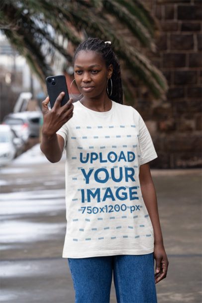Bella Canvas T-Shirt Mockup of a Woman Taking a Selfie with Her Smartphone on the Street