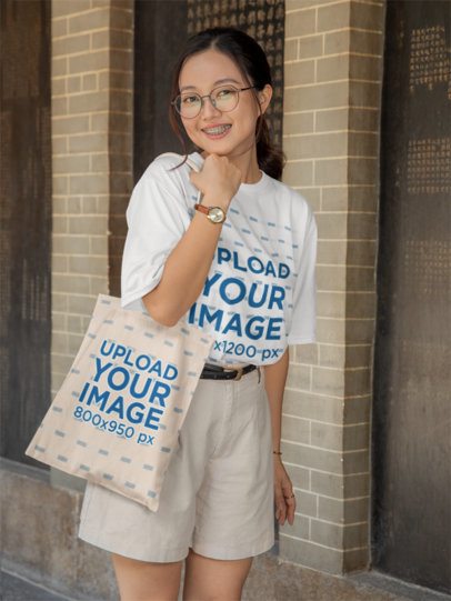 T-Shirt and Tote Bag Mockup of a Happy Woman with Glasses Posing on the Street