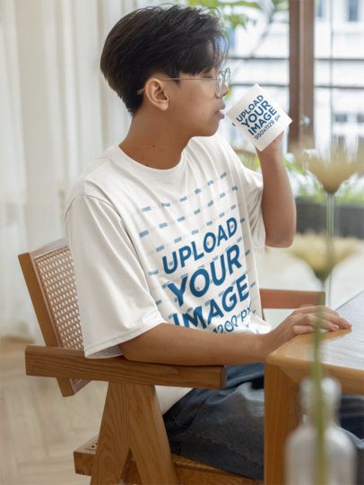 Oversized T-Shirt Mockup Featuring a Teenage Boy Drinking From a Coffee Mug in a Dining Room