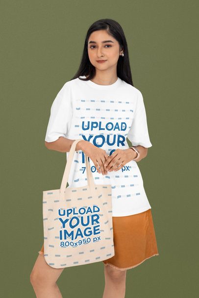 Oversized T-Shirt Mockup Featuring a Woman Posing in a Studio With a Sublimated Tote Bag