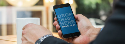 Mockup of a Businessman Holding an iPhone at a Coffee Shop Outdoors Wide