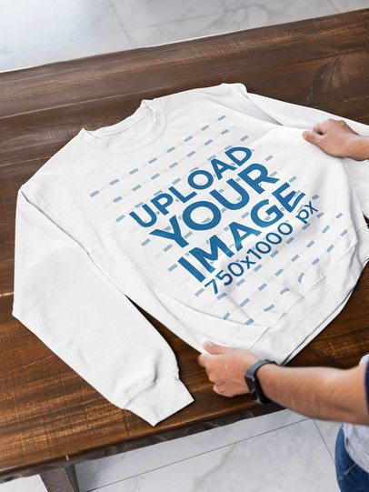 Mockup of a Man Putting a Gildan Sweatshirt Over a Wooden Table m52003