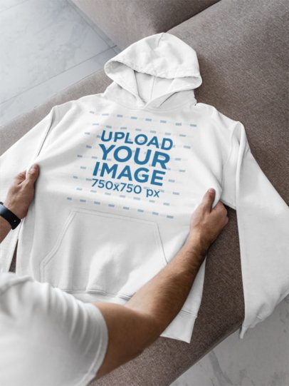 Gildan Mockup Featuring a Man Putting a Pullover Hoodie Over a Couch