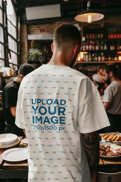 Back-View T-Shirt Mockup Featuring an AI-Created Tattooed Man Standing in a Restaurant