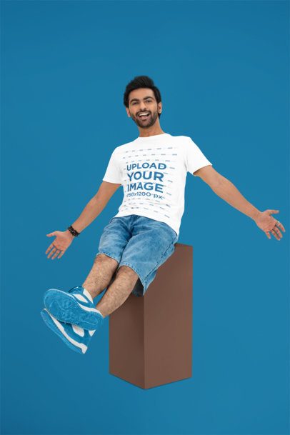 Round-Neck T-Shirt Mockup of a Cheerful Man Sitting on a Cube in a Studio