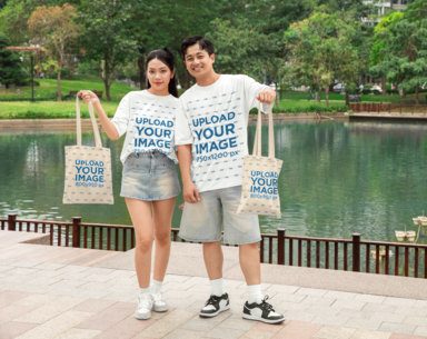 Oversized T-Shirt Mockup of a Smiling Couple Posing in the Park With Sublimated Tote Bags
