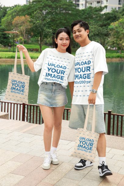 Oversized T-Shirt Mockup Featuring a Happy Sweet Couple Holding Tote Bags in a Park