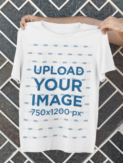 Bella Canvas Mockup Featuring Man's Hands Holding a Round-Neck Tee Against a Wall