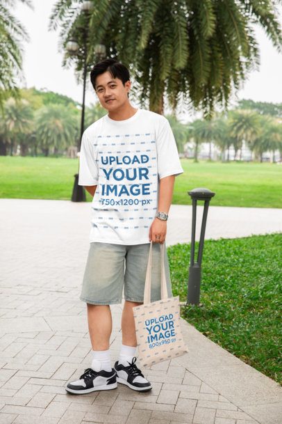 Oversized T-Shirt Mockup of a Happy Man Carrying a Tote Bag at the Park m53759