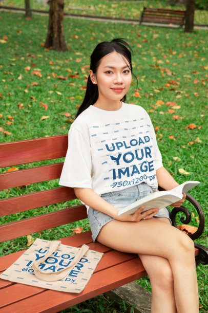 Oversized Tee and Tote Bag Mockup of a Smiling Woman Sitting on a Bench While Reading