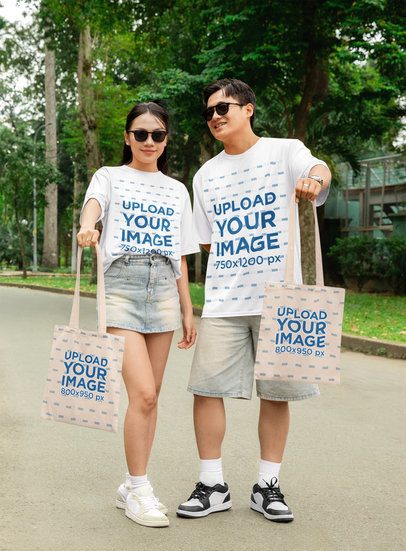 Oversized T-Shirt and Tote Bag Mockup of a Happy Couple Posing in a Park in Matching Outfits