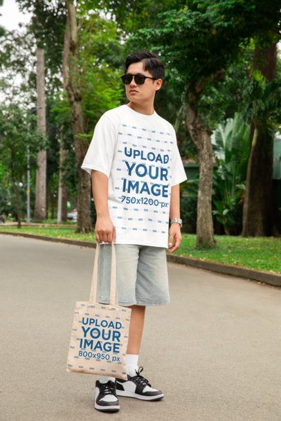 Oversized T-Shirt Mockup Featuring a Serious Man Standing in a Park With a Tote Bag