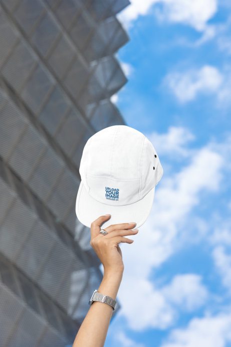 Yupoong Mockup Featuring a Woman's Hand Holding a Panel Cap Hat Against the Sky