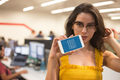 Mockup of a Woman with a Yellow Garment Holding a Silver iPhone 8+ Mockup