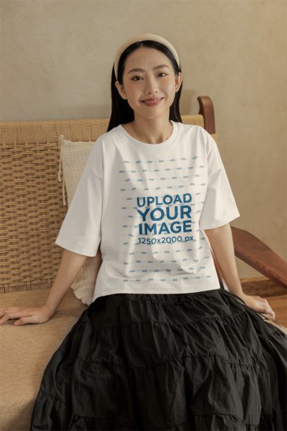 Oversized T-Shirt Mockup of a Smiling Woman Posing in a Cozy Couch