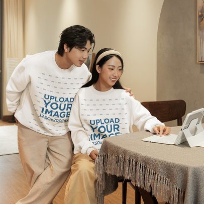 Oversized Sweatshirt Mockup of a Happy Man and a Woman Looking at a Tablet in a Cozy Room