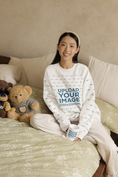 Sweatshirt Mockup Featuring a Happy Woman With a Coffee Mug Sitting on a Cozy Bed