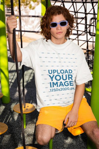 Oversized T-Shirt Mockup of a Man With Sunglasses Sitting in a Playground Game
