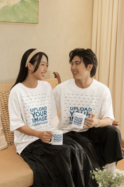 Oversized T-Shirt Mockup of a Cheerful Couple Holding Coffee Mugs in a Cozy Room