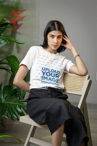 Bella Canvas T-Shirt Mockup Featuring a Woman Sitting on a Chair With Some Plants in the Back m54673