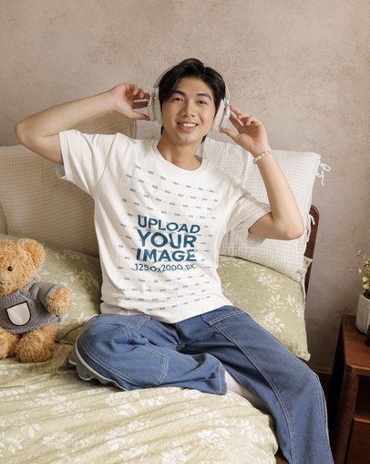 Round-Neck T-Shirt Mockup of a Happy Man With Headphones Sitting in a Cozy Bed