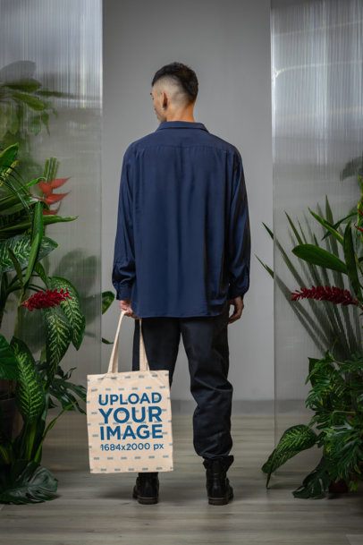 Mockup of a Man Posing Backwards With a Tote Bag in a Secret Garden-Inspired Setting m54663