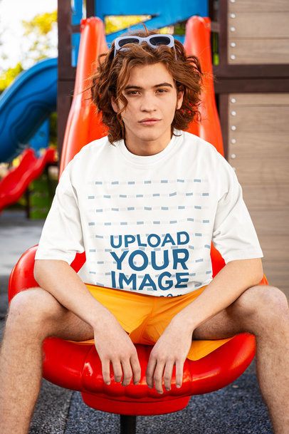 Oversized T-Shirt Mockup of a Serious Man Sitting on a Playground Slide