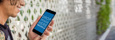 Young Man Using an iPhone 6 Plus and Leaning on Fence