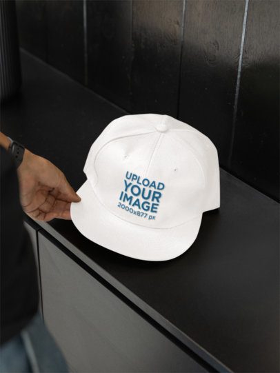 Mockup of a Man Putting a Snapback Hat Over a Dark Drawer