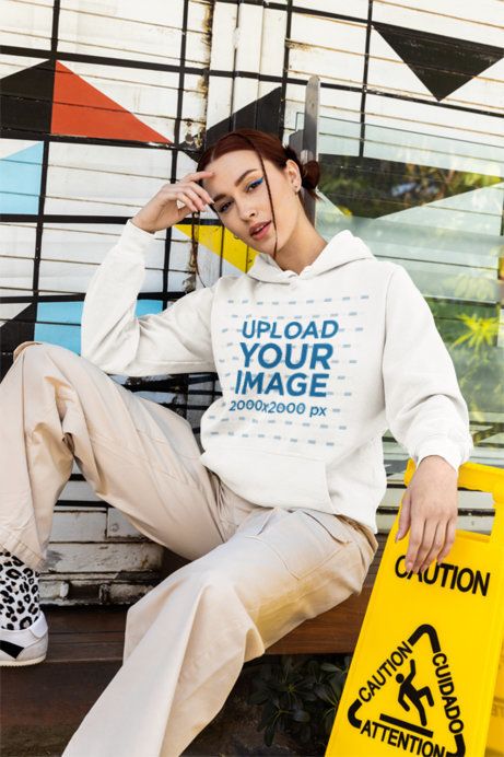 Comfort Colors Hoodie Mockup Featuring a Woman Sitting on the Sidewalk Next to a Caution Sign