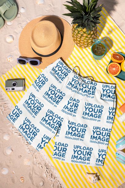 Mockup of Sublimated Swim Shorts Lying on the Sand Featuring Fruits and a Drink