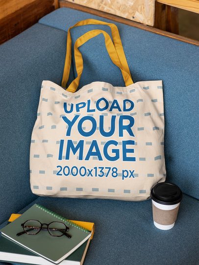 Econscious Mockup Featuring a Tote Bag Lying on a Couch With a Book and a Coffee m56511