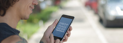 Mockup of a Young Man on a Sidewalk Using a Black iPhone 6
