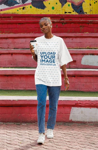Oversized T-Shirt Mockup of a Calm Woman Walking in the Street With Earphones
