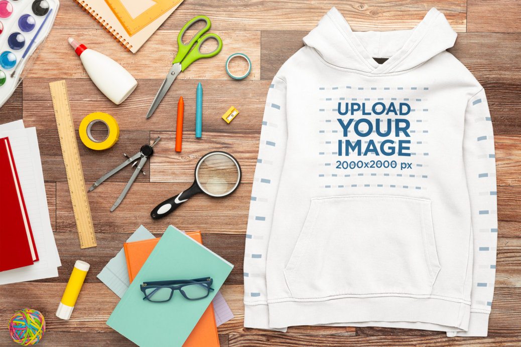 Mockup Hoodie With Customizable Sleeves Lying on a Wooden Surface With School Stuff