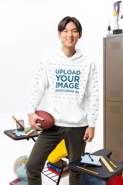 Comfort Colors Hoodie Mockup Featuring a Young Happy Man With a Ball Posing Near Classroom Lockers m57182